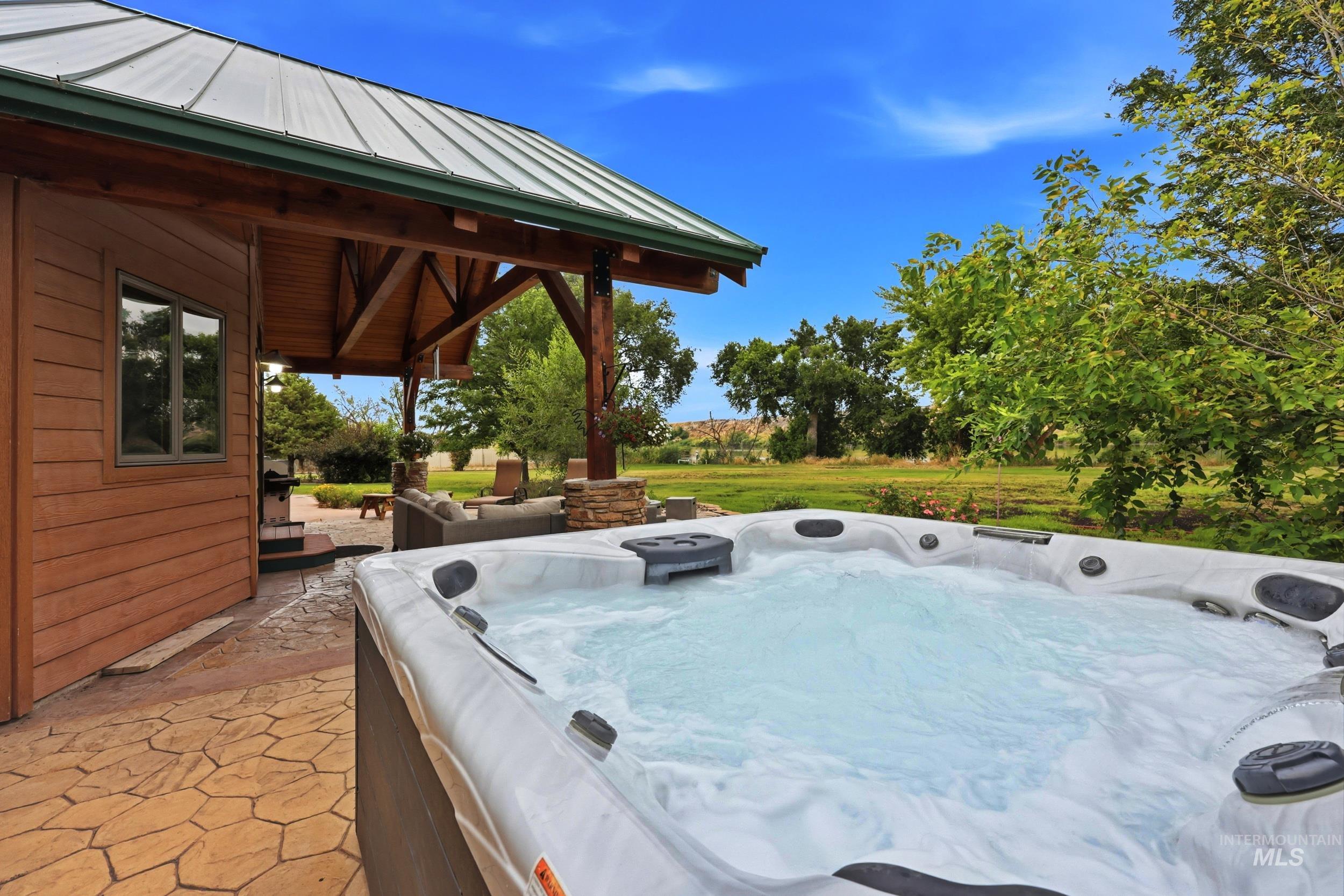 339 Airport Road Weiser, ID 83672 - Photo 34 of 49 Outdoor spa tub, stamped concrete patio, wood-sided exterior, exposed wood beam ceiling, and metal roof