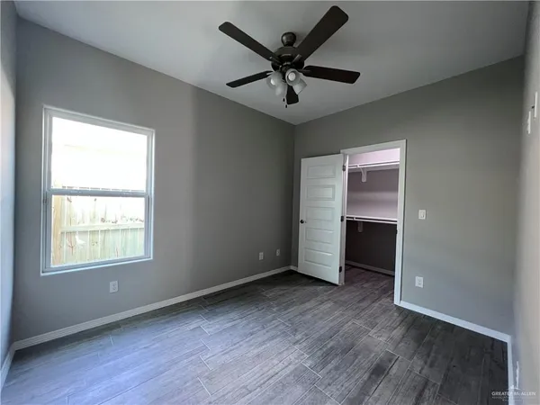 an empty room with wooden floor chandelier fan and windows