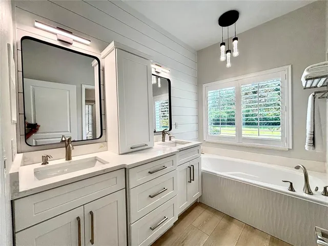 a bathroom with a double vanity sink bathtub and next to a window
