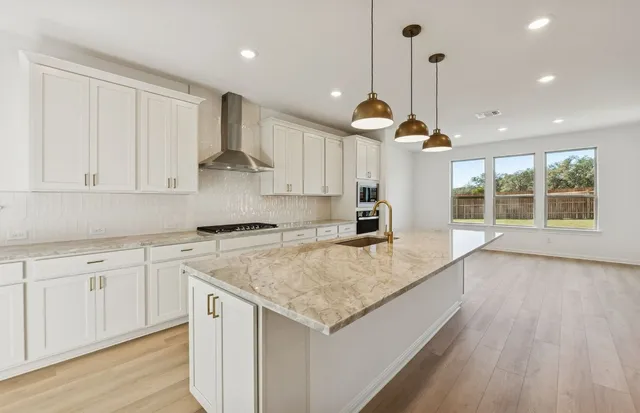 a kitchen with stainless steel appliances granite countertop wooden floors sink stove and white cabinets