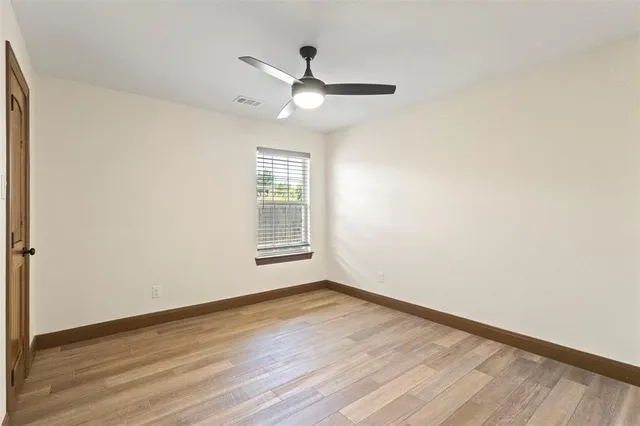 an empty room with wooden floor chandelier fan and windows