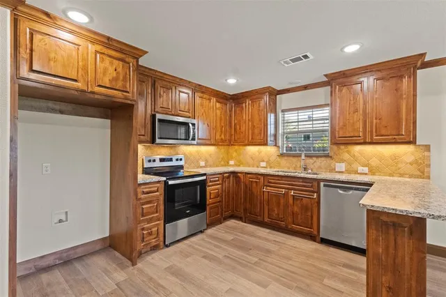 a kitchen with stainless steel appliances granite countertop a stove top oven a sink dishwasher and a refrigerator with wooden cabinets