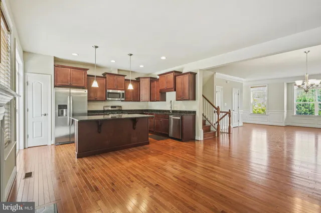a kitchen with stainless steel appliances kitchen island granite countertop wooden floors and view of living room