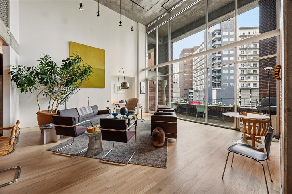 Two-story window wall with city backdrop, complemented by light wood-finish flooring and a concrete ceiling