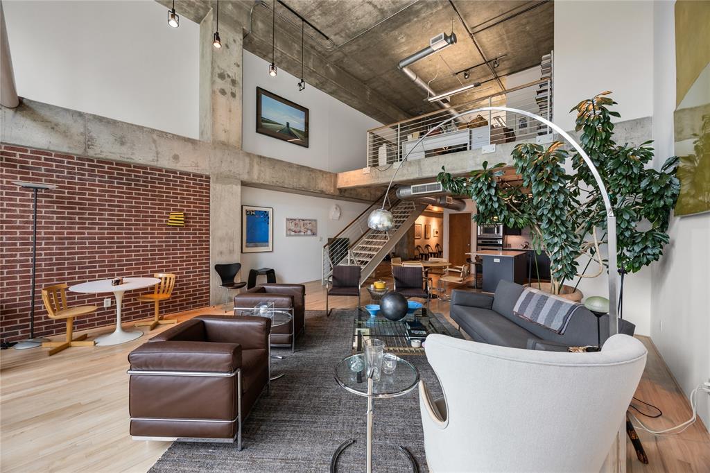 2011 Cedar Springs Road, Unit 305 Dallas, TX 75201 - Photo 13 of 27 Expansive open-concept living space featuring high ceilings, exposed brick accents, concrete structural elements, a visible mezzanine level, and light wood-finish flooring