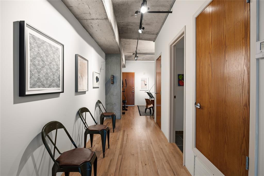 2011 Cedar Springs Road, Unit 305 Dallas, TX 75201 - Photo 2 of 27 Hardwood flooring throughout a hallway featuring exposed concrete ceilings, track lighting, and solid core doors with brushed nickel hardware