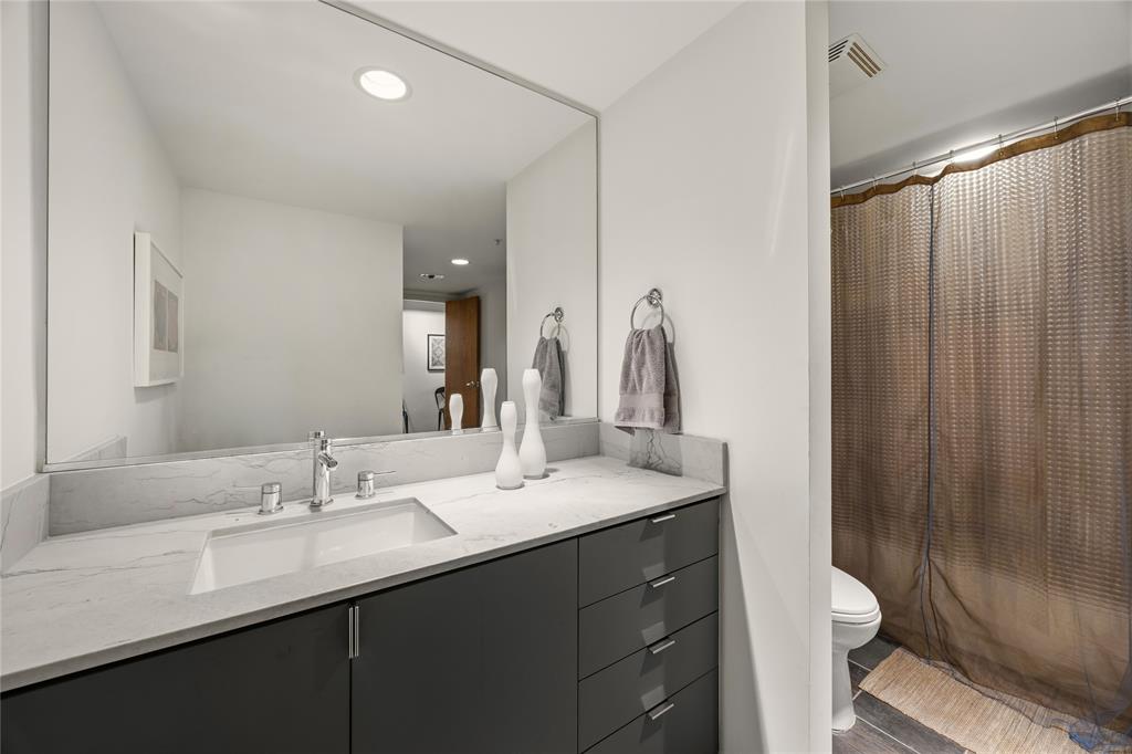 2011 Cedar Springs Road, Unit 305 Dallas, TX 75201 - Photo 23 of 27 Bathroom featuring a dark gray vanity with chrome hardware, an integrated rectangular sink, a light-toned countertop with veining, a large wall-mounted mirror, and recessed lighting