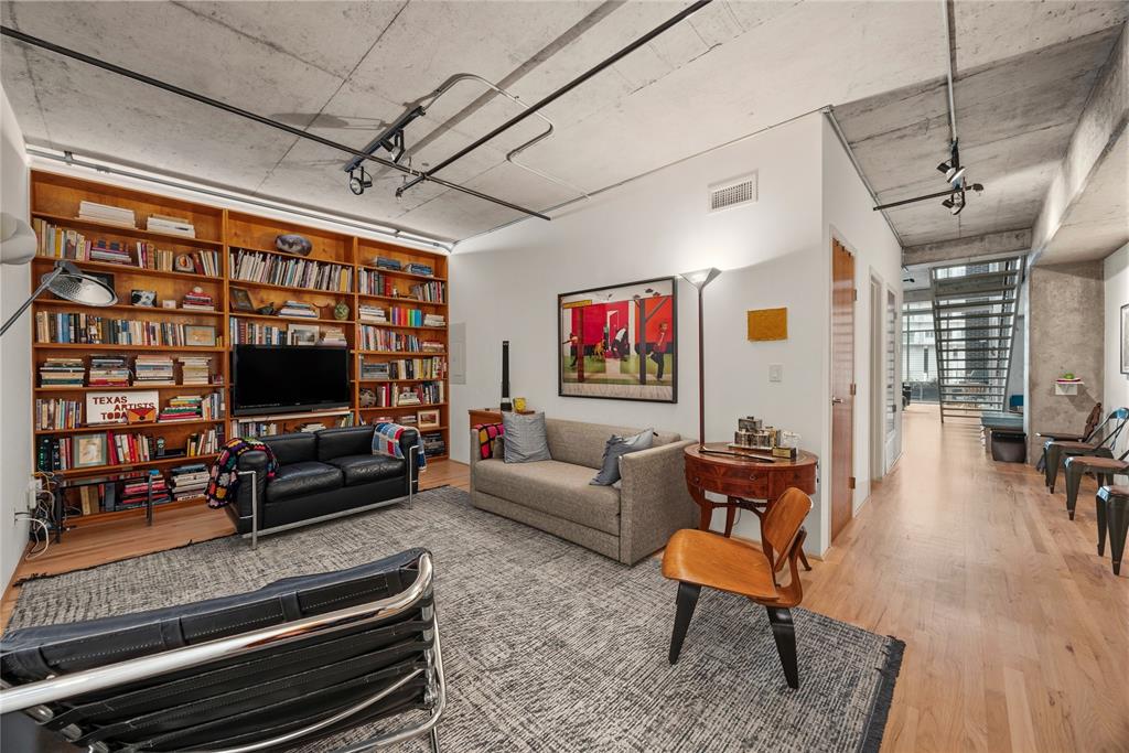 2011 Cedar Springs Road, Unit 305 Dallas, TX 75201 - Photo 3 of 27 Open-concept living area featuring extensive built-in wooden shelving, exposed concrete ceilings with industrial-style track lighting, light wood-finish flooring, and white walls