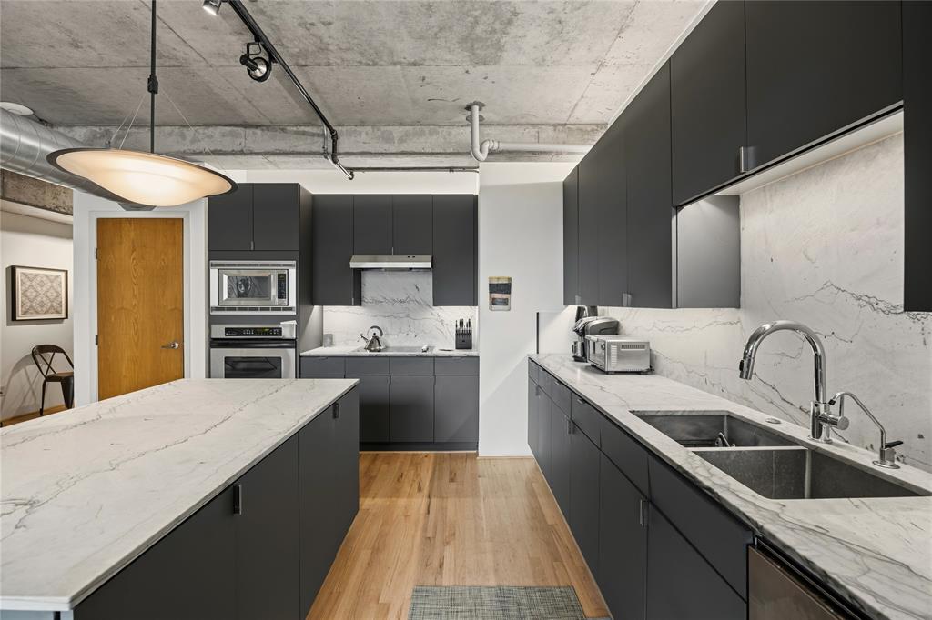 2011 Cedar Springs Road, Unit 305 Dallas, TX 75201 - Photo 8 of 27 Modern kitchen featuring a large island with a white veined countertop, dark flat-panel cabinetry, light wood-finish flooring, stainless steel appliances, and track lighting