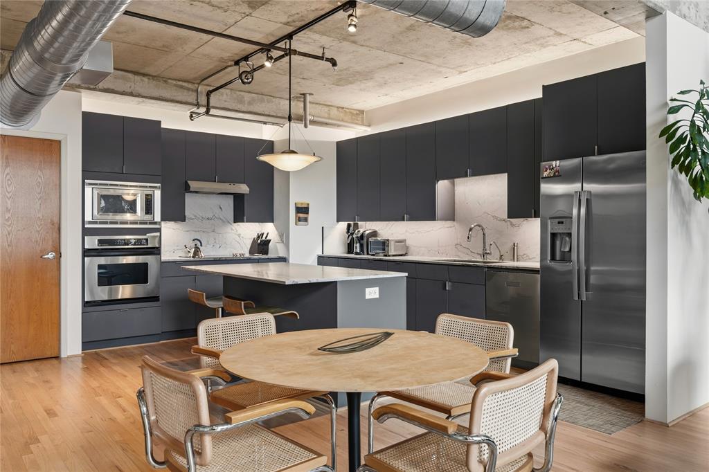 2011 Cedar Springs Road, Unit 305 Dallas, TX 75201 - Photo 9 of 27 Contemporary kitchen featuring industrial-style exposed ductwork and track lighting, dark flat-panel cabinetry, stainless steel appliances, and a central island with a light-toned countertop