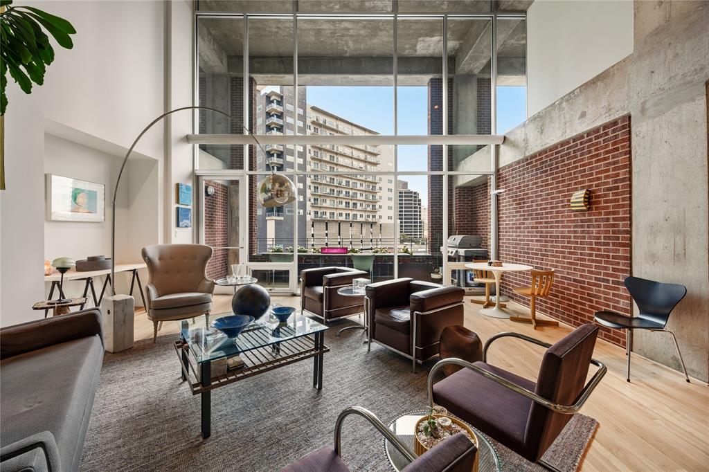 2011 Cedar Springs Road, Unit 305 Dallas, TX 75201 - Photo 10 of 27 Spacious living area featuring floor-to-ceiling windows, exposed concrete ceilings, a brick accent wall, light wood-finish flooring, and a private balcony