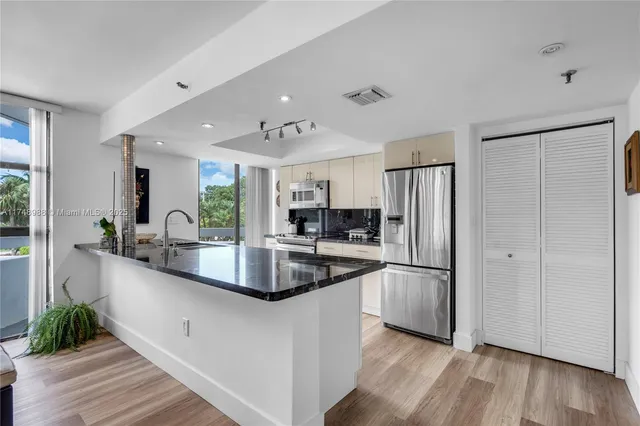 a kitchen with stainless steel appliances granite countertop a refrigerator a sink and white cabinets