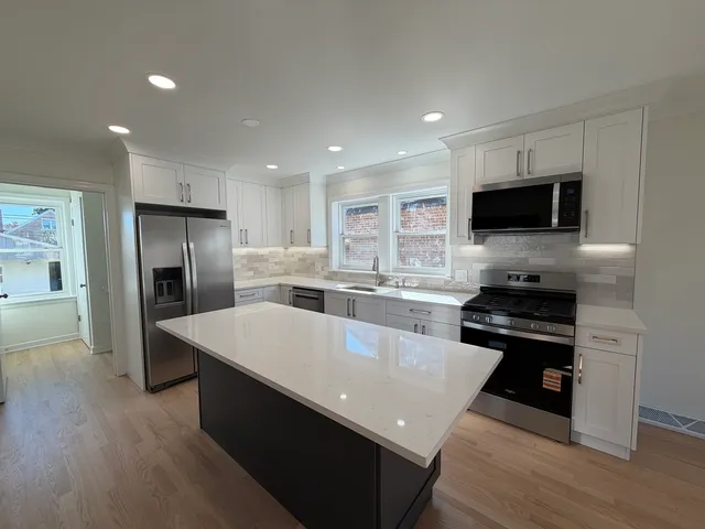 a large kitchen with stainless steel appliances kitchen island granite countertop a stove a refrigerator a sink a oven and a dining table with wooden floor