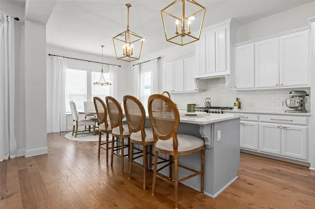 a kitchen with stainless steel appliances granite countertop a dining table chairs stove and white cabinets