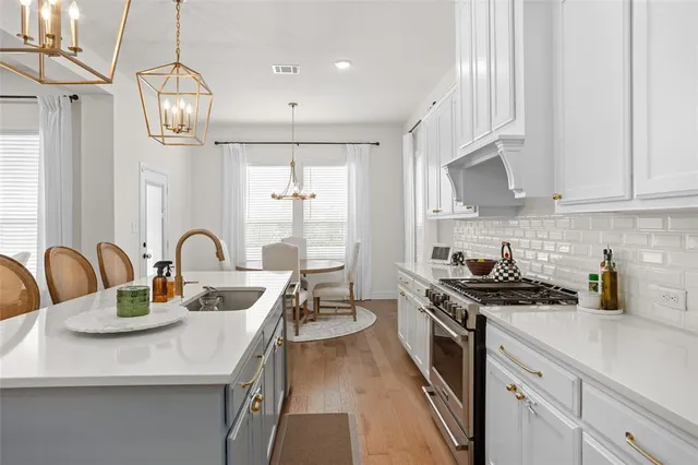 a kitchen with stainless steel appliances granite countertop a sink a stove a window cabinets and a dining table