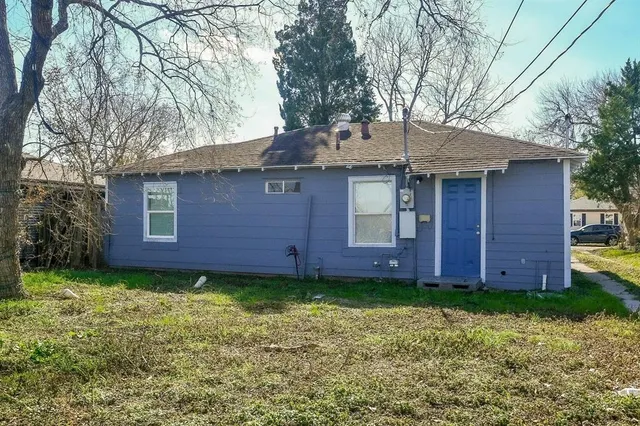 a view of a brick house with a big yard plants and large tree
