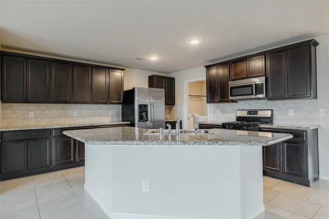 a kitchen with kitchen island granite countertop stainless steel appliances a sink a stove a microwave and wooden cabinets