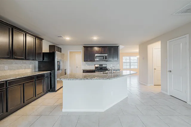 a large kitchen with stainless steel appliances kitchen island granite countertop a refrigerator and a sink