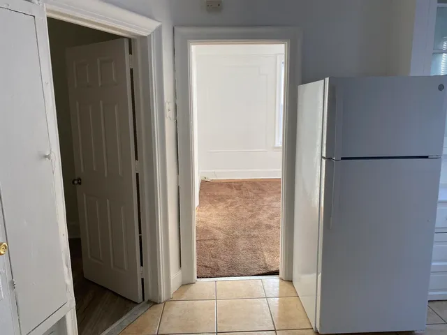 a view of a refrigerator in kitchen and an empty room