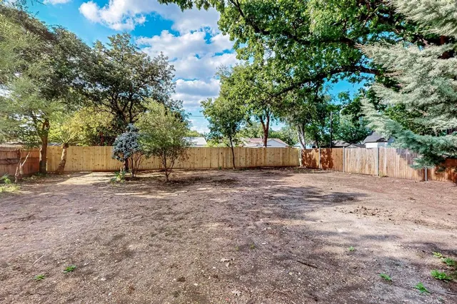 a view of a backyard with large trees and wooden fence