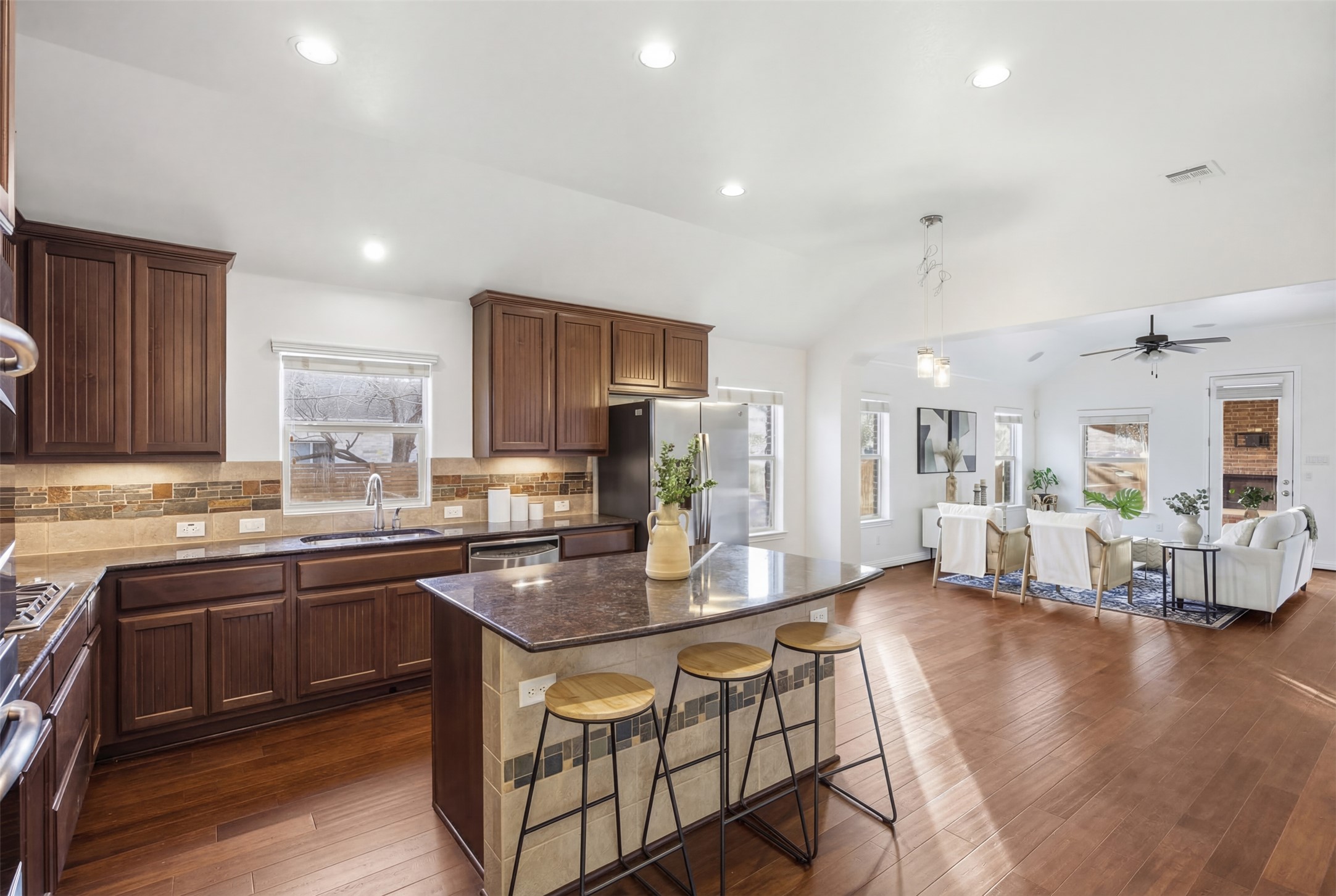 a kitchen with stainless steel appliances granite countertop a stove top oven a sink dishwasher a dining table and chairs with wooden floor