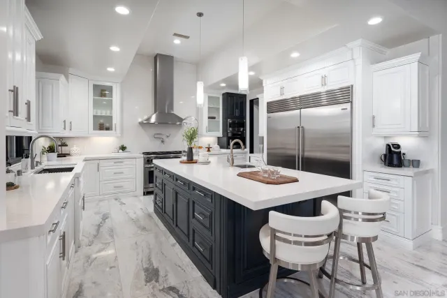 a kitchen with stainless steel appliances kitchen island granite countertop a sink a stove a refrigerator and white cabinets with wooden floor