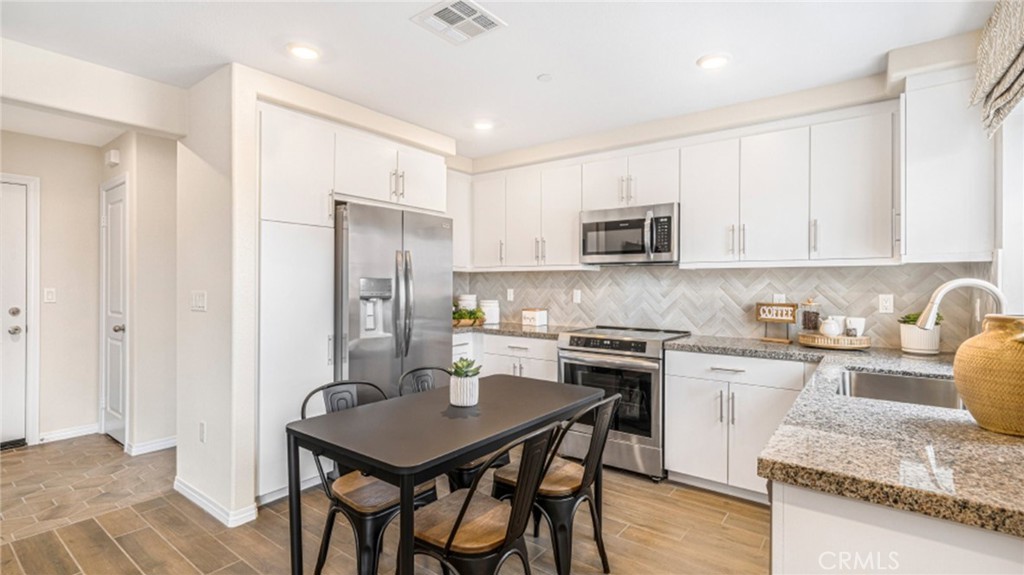 a kitchen with granite countertop kitchen island stainless steel appliances a stove refrigerator a sink a stove a dining table and chairs with wooden floor