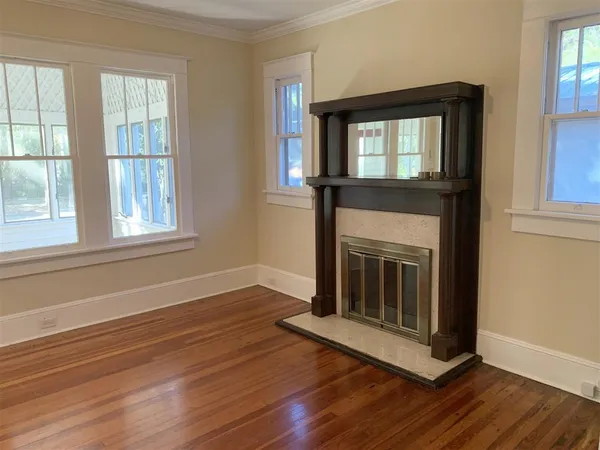 a view of an empty room with wooden floor fireplace and a window