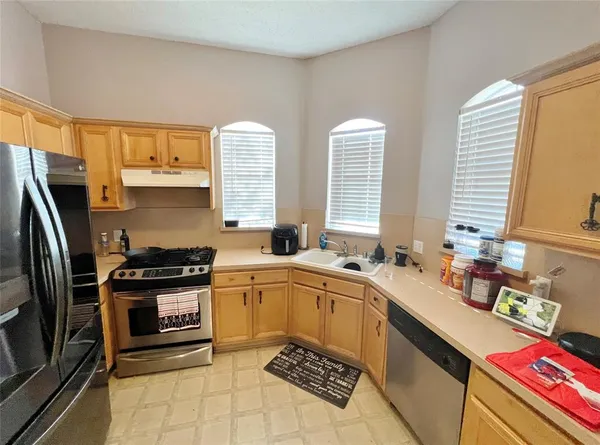 a kitchen with stainless steel appliances a sink a stove a refrigerator cabinets and a window