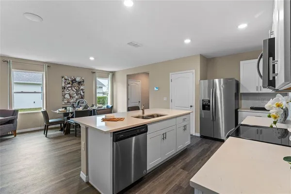 a kitchen with stainless steel appliances granite countertop a refrigerator a sink dishwasher a dining table and chairs with wooden floor