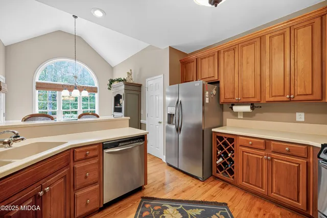 a kitchen with stainless steel appliances granite countertop a refrigerator a sink dishwasher and wooden cabinets with wooden floor