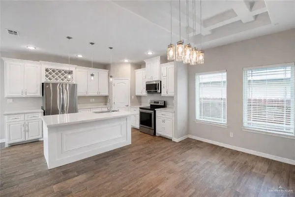 a large white kitchen with granite countertop a stove top oven a sink dishwasher and white cabinets with wooden floor