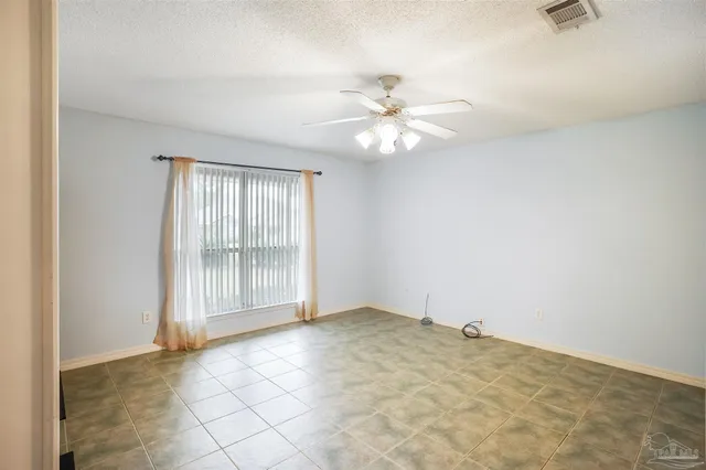 an empty room with chandelier fan and windows
