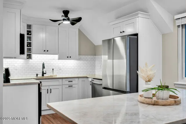 a kitchen with stainless steel appliances kitchen island granite countertop a refrigerator a sink a stove and white cabinets