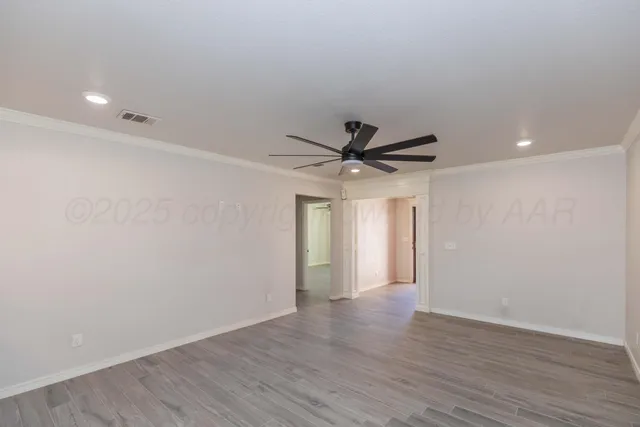 a view of an empty room with wooden floor and a ceiling fan