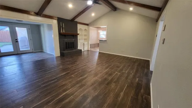 an empty room with wooden floor and a kitchen