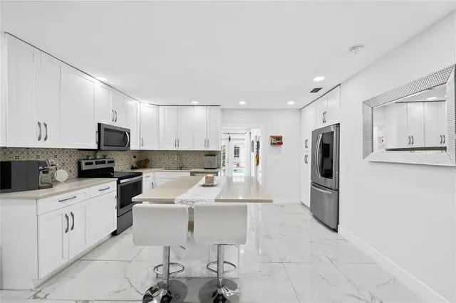 a large white kitchen with stainless steel appliances kitchen island granite countertop a refrigerator and a stove top oven