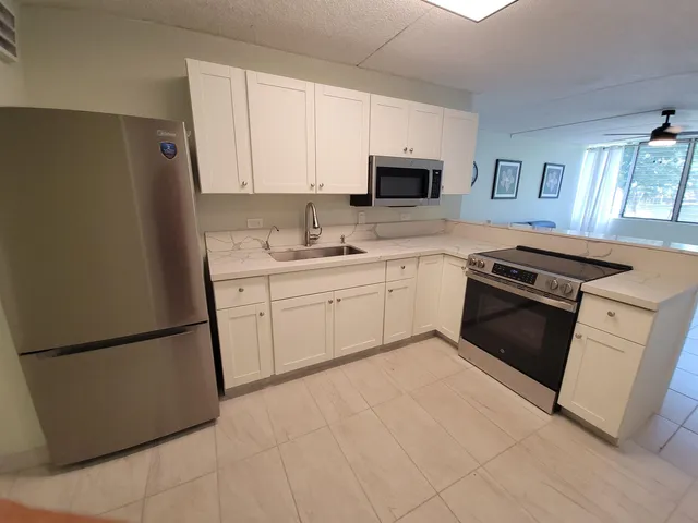 a kitchen with stainless steel appliances granite countertop white cabinets a sink a stove a refrigerator and white cabinets