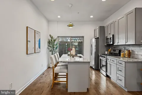 a kitchen with stainless steel appliances kitchen island granite countertop a stove a sink a refrigerator and white cabinets with wooden floor