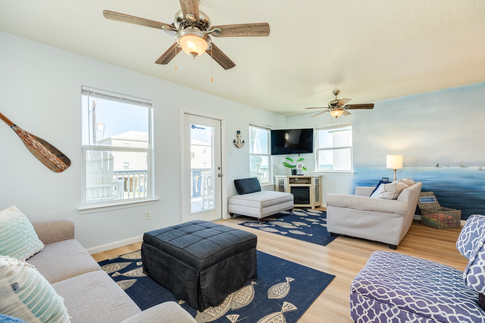 107 Howard Avenue Surfside Beach, TX 77541 - Photo 19 of 38 Bright and inviting living area featuring coastal-inspired décor, wood-look flooring, and abundant natural light from multiple windows and balcony access.