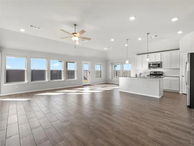 a view of an empty room with kitchen appliances and a ceiling fan