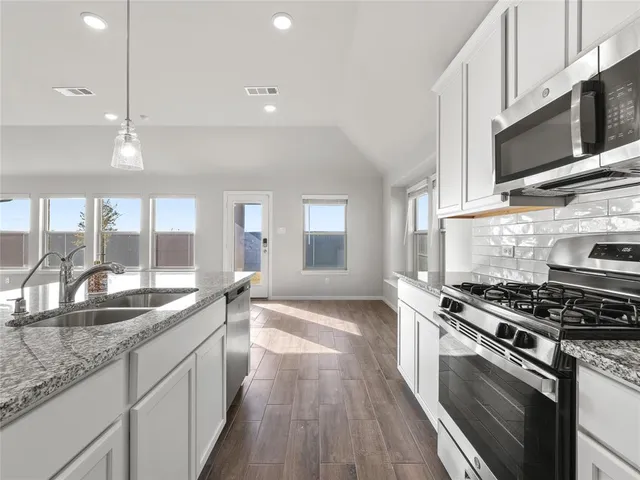 a kitchen with stainless steel appliances kitchen island granite countertop a sink a stove and a wooden floors