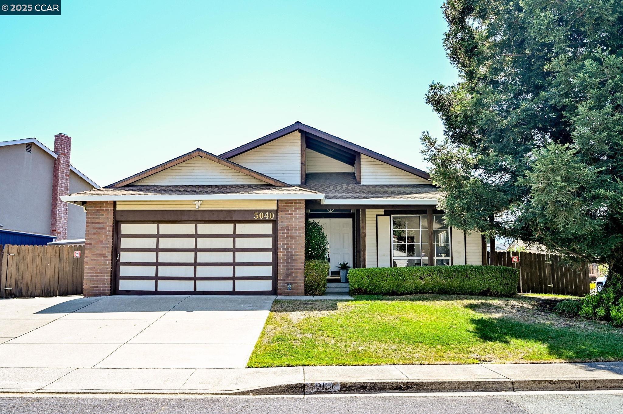 a view of a white house with a large yard plants and large tree