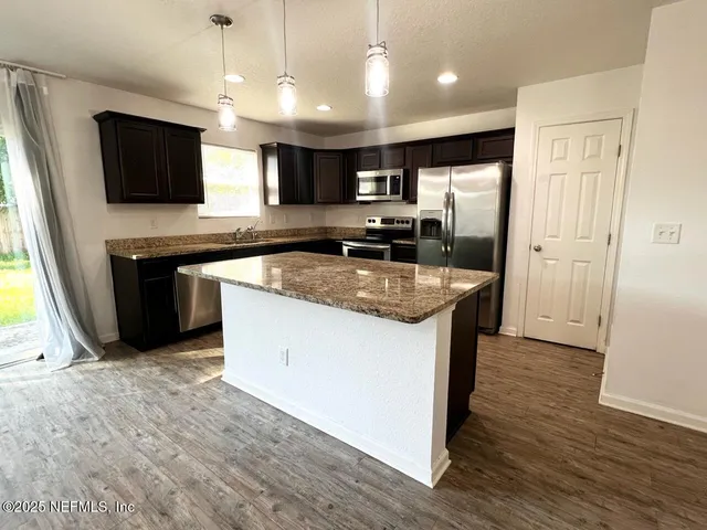 a kitchen with stainless steel appliances granite countertop a stove top oven a sink dishwasher a refrigerator and a dining table with wooden floor
