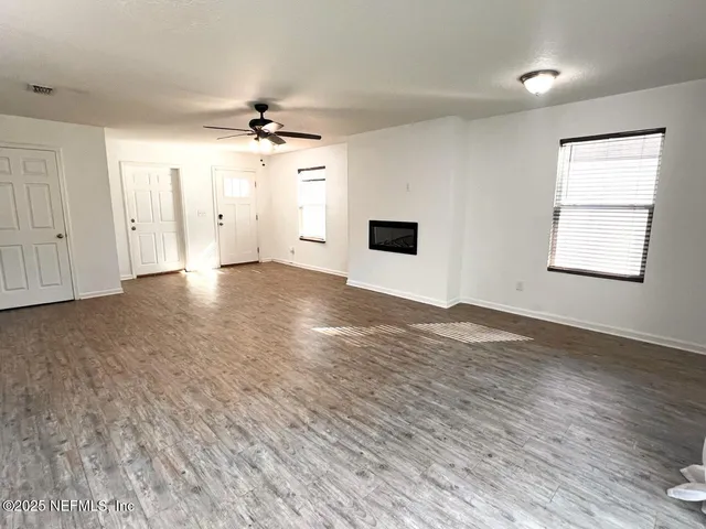an empty room with wooden floor ceiling fan and windows