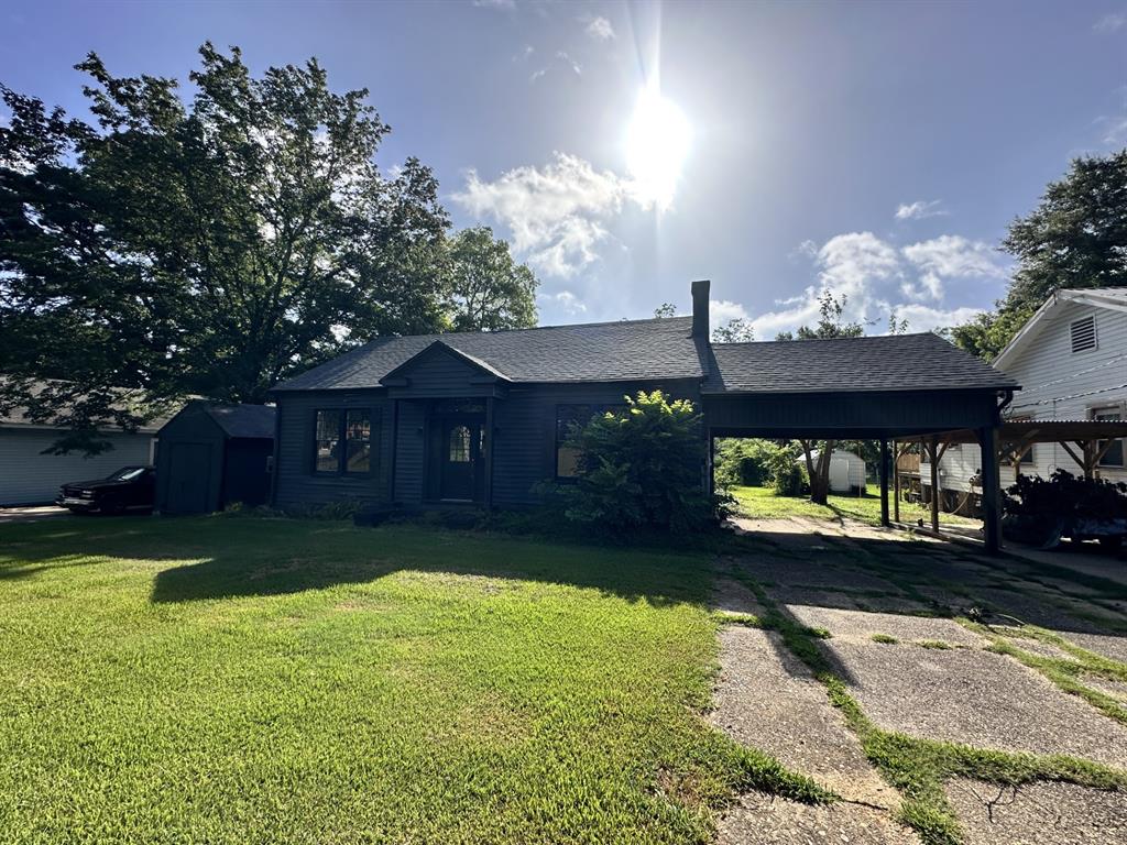 View of front of house with a shed, a shingled roof, a carport, a front yard, and driveway