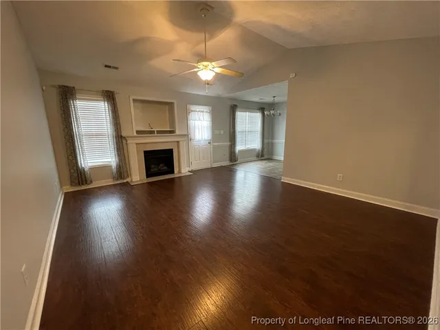 an empty room with wooden floor fireplace and windows