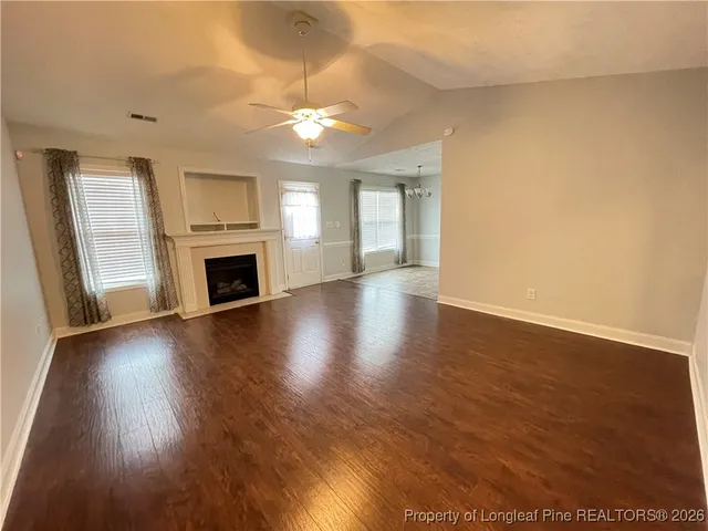 an empty room with wooden floor fireplace and windows
