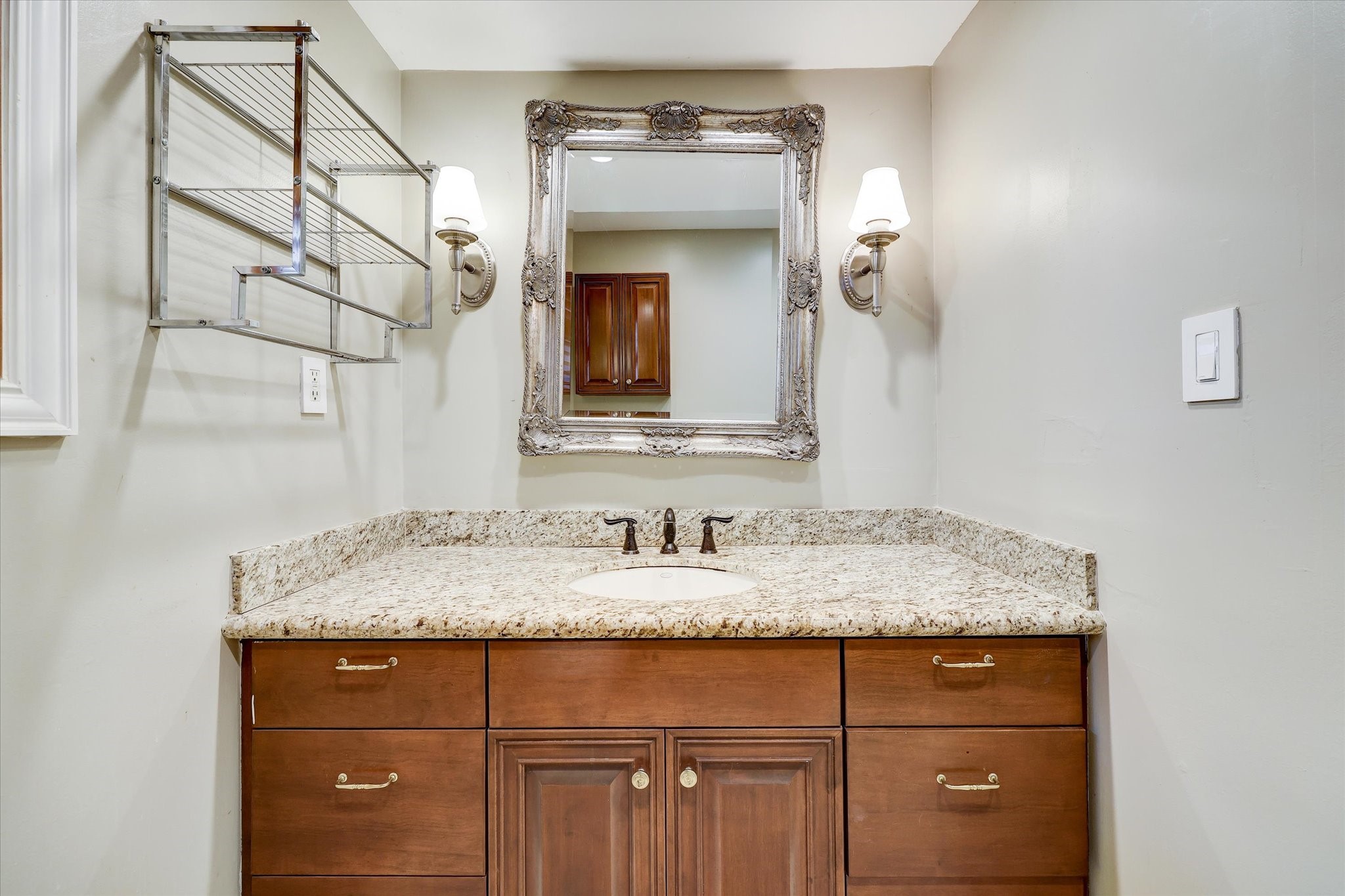 2401 Maconda Lane Houston, TX 77027 - Photo 12 of 20 Closer view of the Primary Bath with stained cabinets/drawers below, granite counter/backsplash, decorative fixtures, mirror flanked by decorative sconces, metal shelving, window.