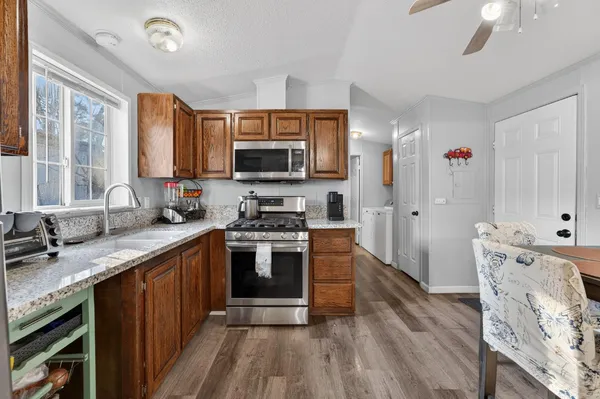 a kitchen with stainless steel appliances a stove top oven a sink dishwasher a refrigerator and a dining table with wooden floor